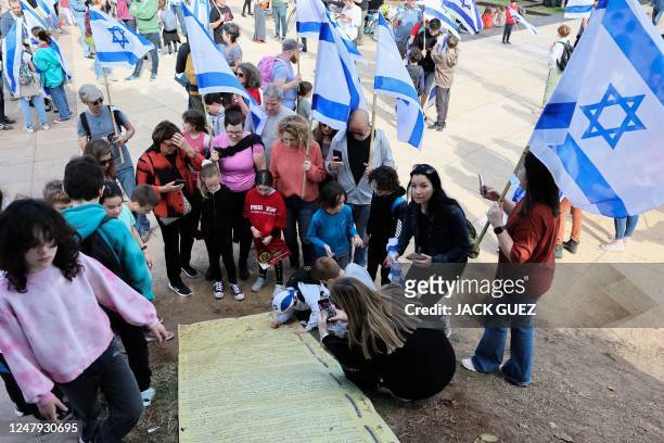 Young Israelis and their parents sign a copy of Israel's 1948 declaration of independence during a protest against government legal reforms which are...