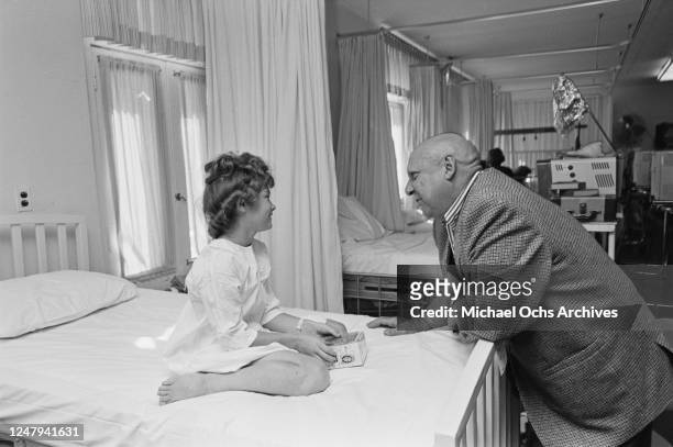 American actor and comedian Jackie Coogan visits a children's hospital in Denver, Colorado, 10th September 1965. The girl is holding an Addams Family...