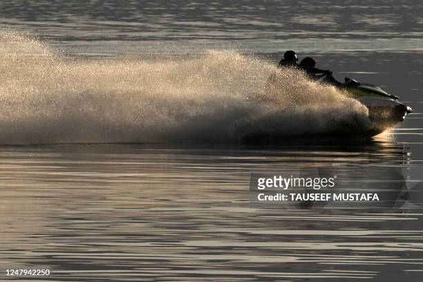 Men ride a water scooter in Dal Lake during sunset in Srinagar on March 9, 2023.