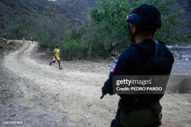 Raramuri runs the "Caballo Blanco" ultramarathon as a state police agent guards, in Urique, in the Tarahumara mountains of the state of Chihuahua,...