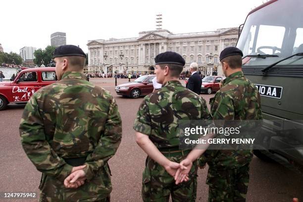 Soldiers keep watch as thousands gather, many American, outside the gates of Buckingham Palace 13 September 2001, as a band from No.7 Company...