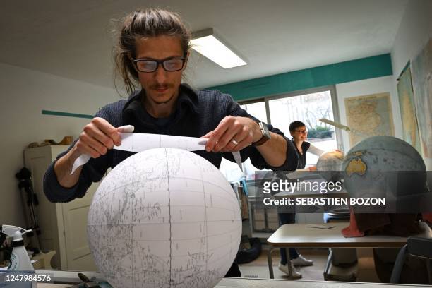 Alain Sauter, hearth globe maker and head of "Globe Sauter" brand, sticks a sheet of printed paper on a globe at the workshop in Besancon, on March...