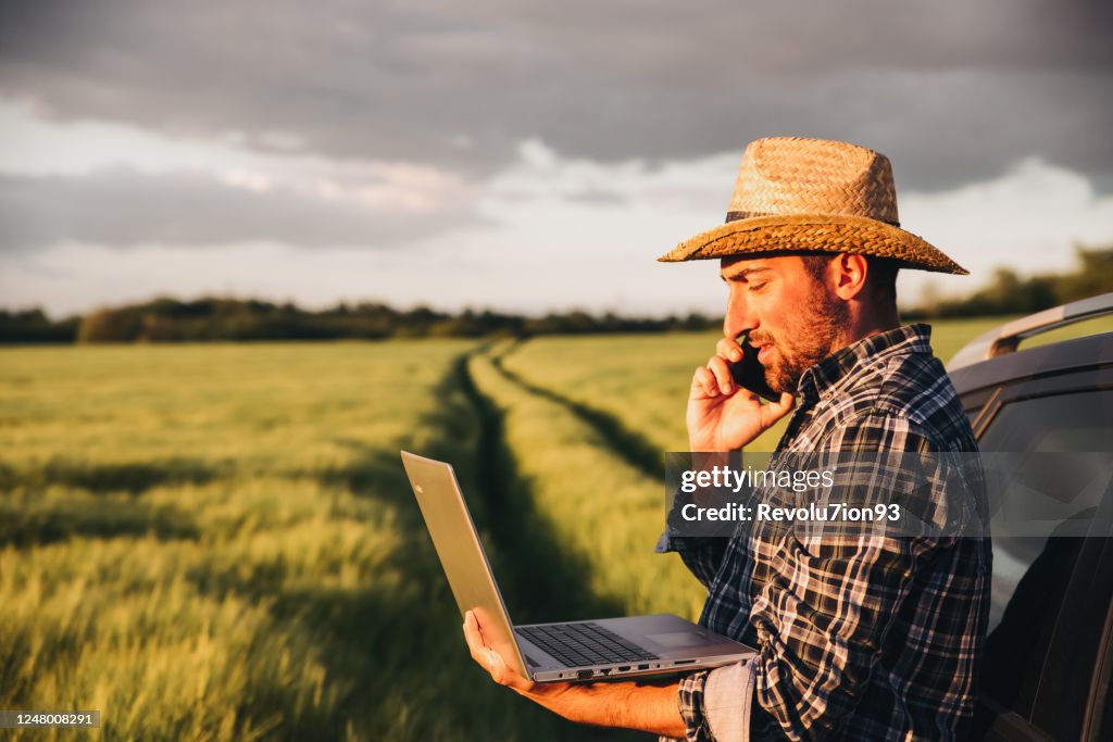 Modern farmer using laptop and smartphone to control the harvest on his field