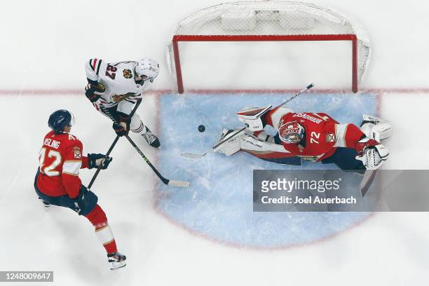 Gustav Forsling of the Florida Panthers checks Lukas Reichel of the Chicago Blackhawks as Sergei Bobrovsky stops his shot during the third period of...