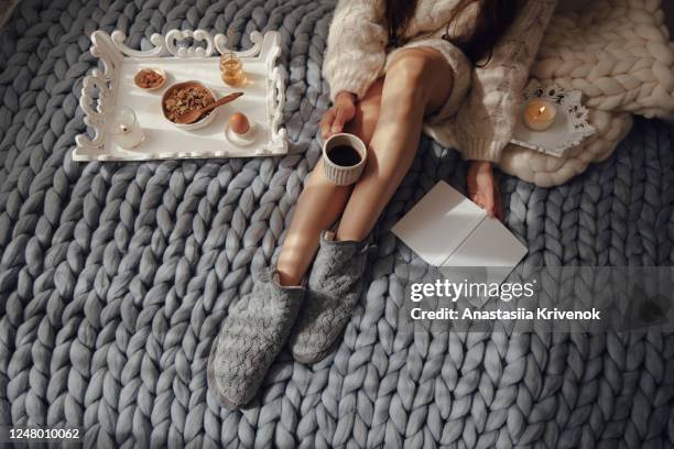 woman with long hair drinking hot coffee and reading book in bed. woman in woolen socks and sweater sitting on wool chunky merino plaid. cozy winter morning concept. - 美脚 ストックフォトと画像