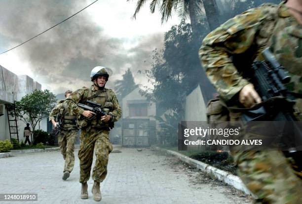 Australian soldiers chase gang members who were setting a house on fire in Dili, 28 June 2006. Stone-throwing youths attacked refugee camps in East...