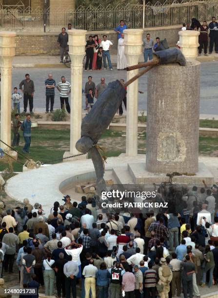 Iraqis watch a statue of Iraqi President Saddam Hussein falling in Baghdad's al-Fardous square 09 April 2003. Iraqis began removing symbols of...