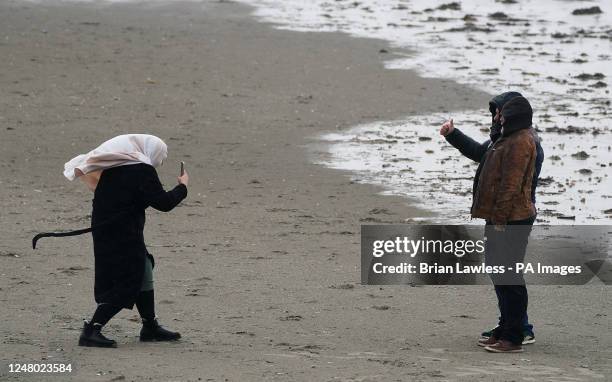 Woman takes pictures on Dollymount strand on a wet and windy day in Dublin. Picture date: Saturday March 11, 2023.