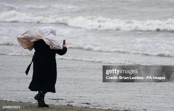 Woman takes pictures on Dollymount strand on a wet and windy day in Dublin. Picture date: Saturday March 11, 2023.