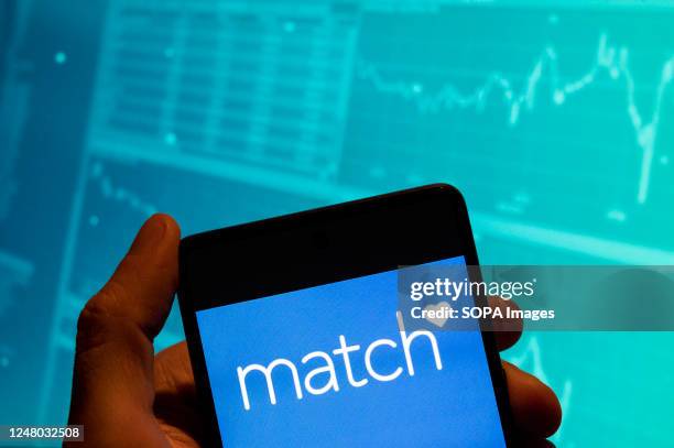 In this photo illustration, the American online dating service Match logo is seen displayed on a smartphone with an economic stock exchange index...