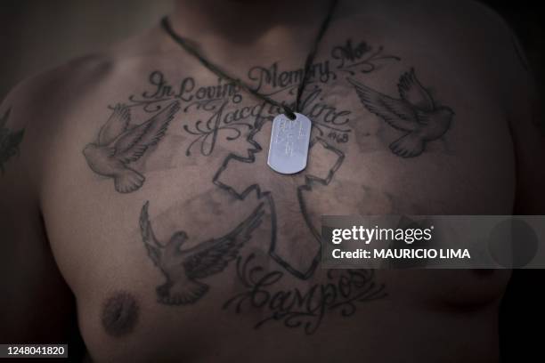 3rd Battalion, 6th Marines, Corporal Lorenzo Robles of Anaheim, California, poses to show his chest tattoo of a cross, doves and the inscription "In...