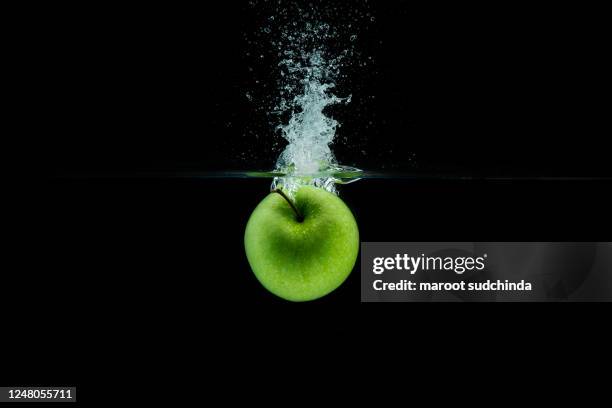 green apple falling in water with splash on black background. - apple water splashing stock pictures, royalty-free photos & images