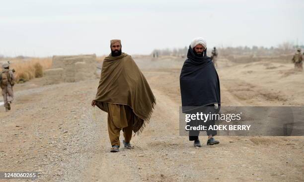 Two local residents wearing the traditional dress shalwar kameez walk past US Marines of the 2nd Batallion, 1st Marines Regiment on patrol in...