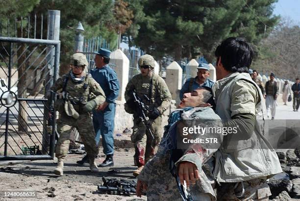 An Afghan man carries a victim of a suicide attack as US soldiers arrive at the site of a suicide attack in Maymana city of Faryab province, north of...