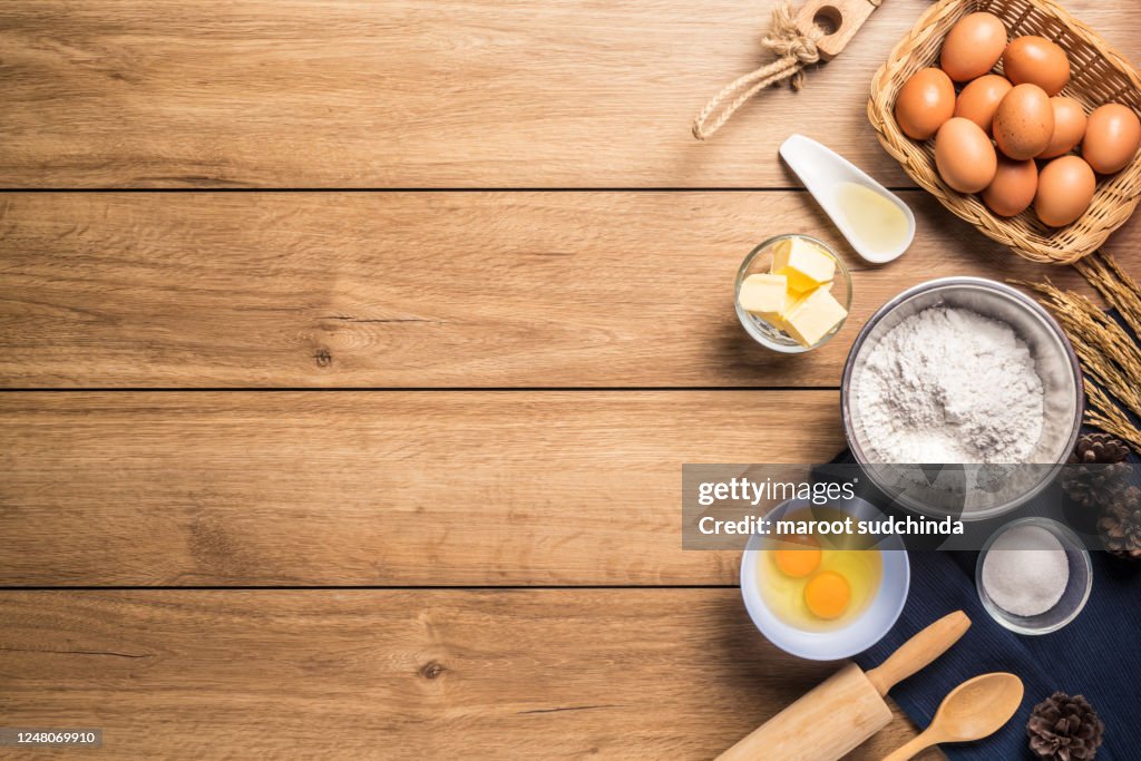 Pictures of ingredients for making cakes bakery around, such as eggs, flour, sugar, butter, powder and equipment for making on a wooden floor, top view, with copy space.