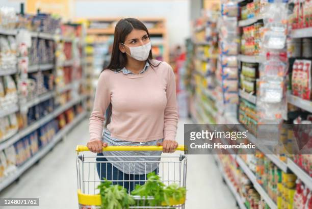 woman grocery shopping at the supermarket wearing a facemask and pushing the car - biosecurity stock pictures, royalty-free photos & images