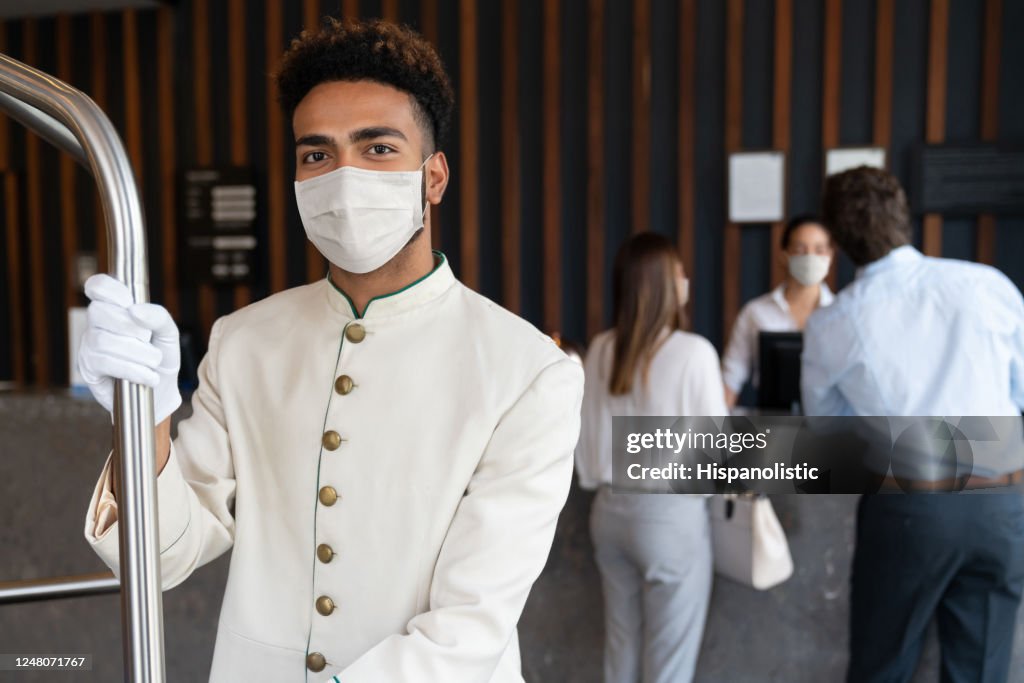 Happy bellboy working at a hotel and wearing a facemask to avoid COVID-19