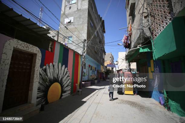 Palestinians walk past the facades of houses painted by artists in Gaza City, on March 12, 2023.