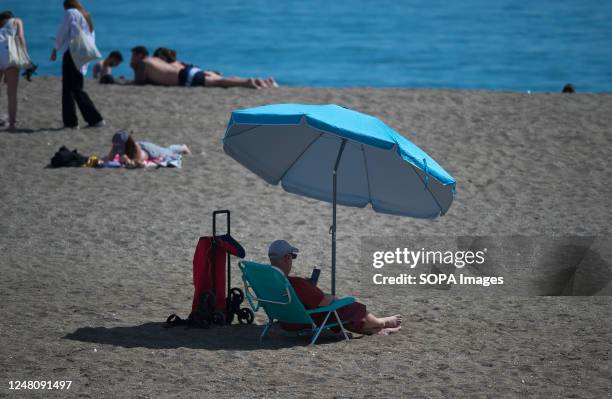 Bather is seen protecting himself from the sun with an umbrella at Malagueta beach during a hot spring day. The good weather and high temperatures...