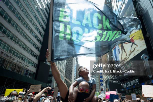 Protester holds a flag with the words Black Housing holds a young protester on his shoulders while she looks at the flag and is among the thousands...