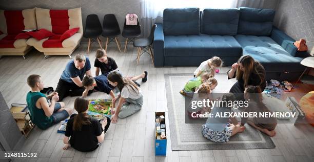 Russian pastor Roman Vinogradov plays a board game on the floor with a group of older children while his wife Yekaterina reads a story to little ones...