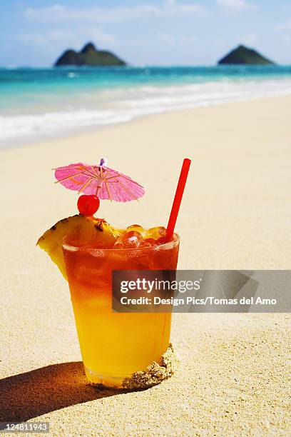 a mai tai garnished with pinapple and a cherry, sitting in the sand on the beach. - mai tai stock-fotos und bilder