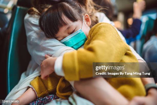 little girl with medical face mask sleeping soundly in mother’s arms while they are riding on bus - child coronavirus sick stock-fotos und bilder