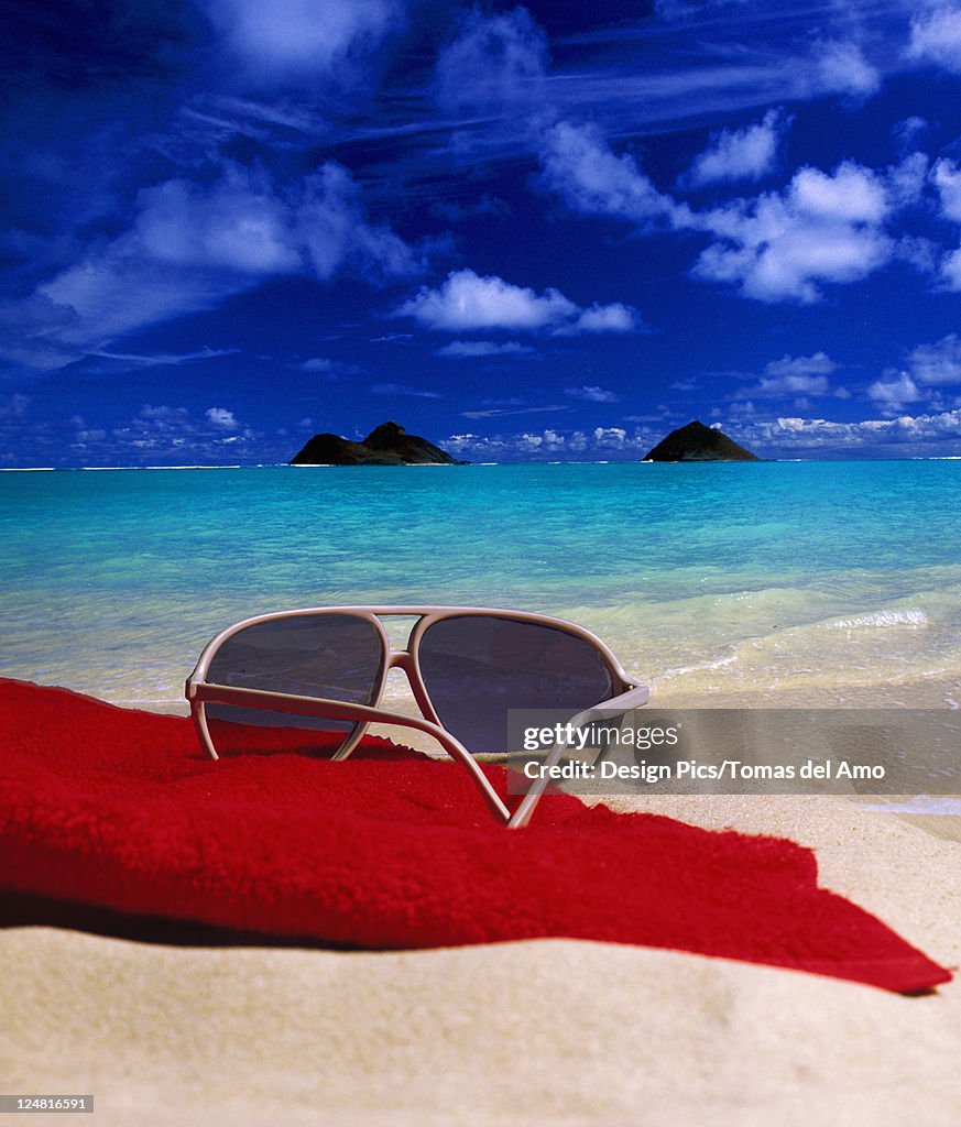Hawaii, Oahu, Lanikai, Sunglasses and red towel in sand on beach, mokulua' || chr(39) || 's in background