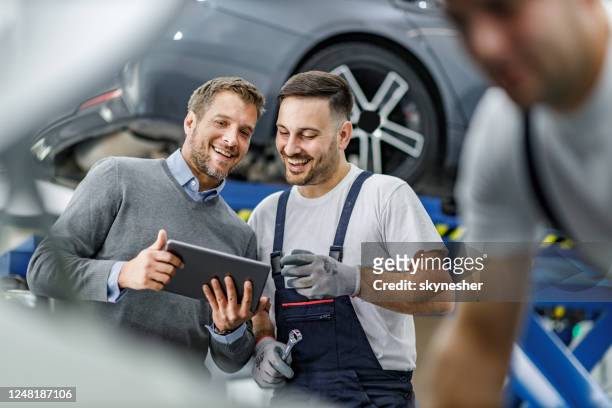 feliz cliente y mecánico de automóviles usando touchpad en un taller. - car workshop fotografías e imágenes de stock