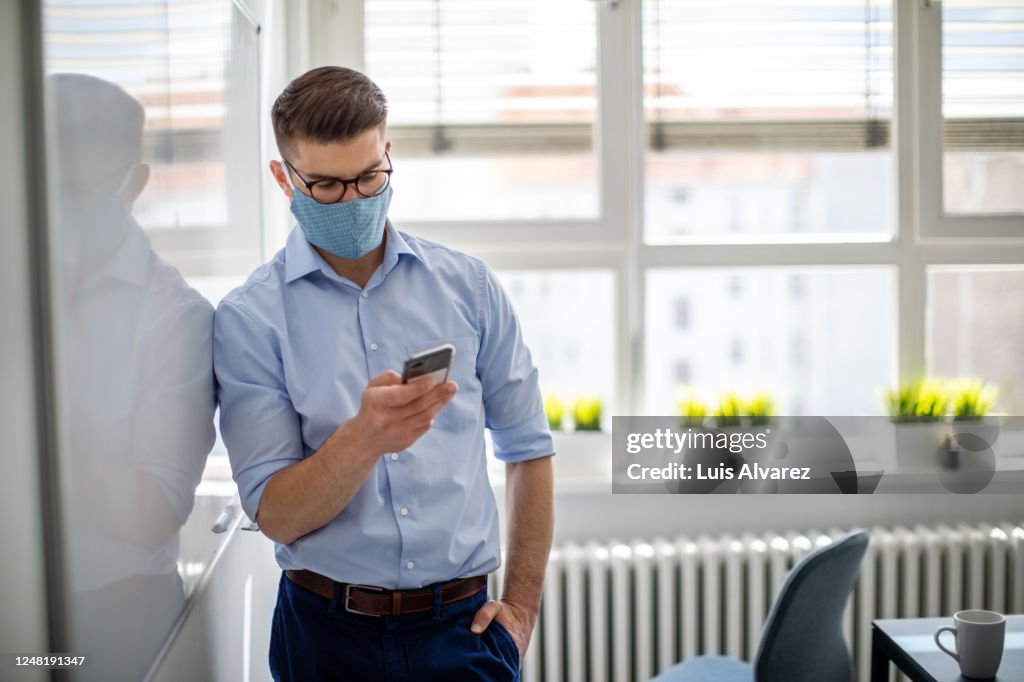 Businessman with face mask in office using mobile phone