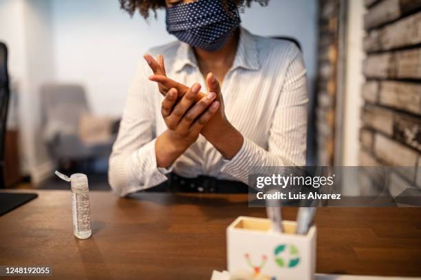 businesswoman sitting at her desk cleaning hands with sanitizer - hand sanitiser - fotografias e filmes do acervo