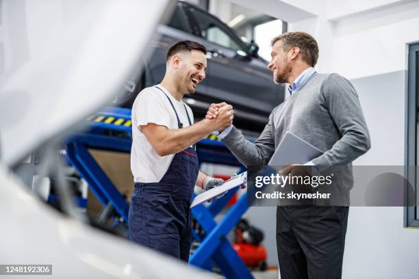 gelukkige automonteur en zijn managergroet in een reparatiewerkplaats. - autobergplaats stockfoto's en -beelden