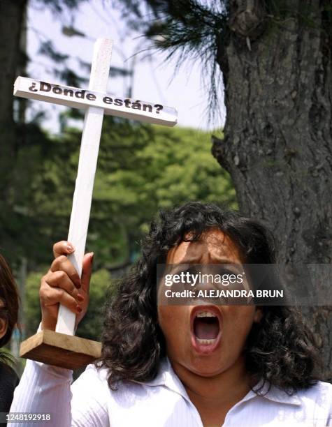 Marisol Barrientos, relative of two victims of political violence, holds a cross which says "Where are they"?, during a protest at the exterior of...