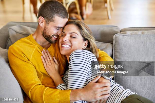 romantic couple embracing on sofa at home - comfortable couple stock pictures, royalty-free photos & images
