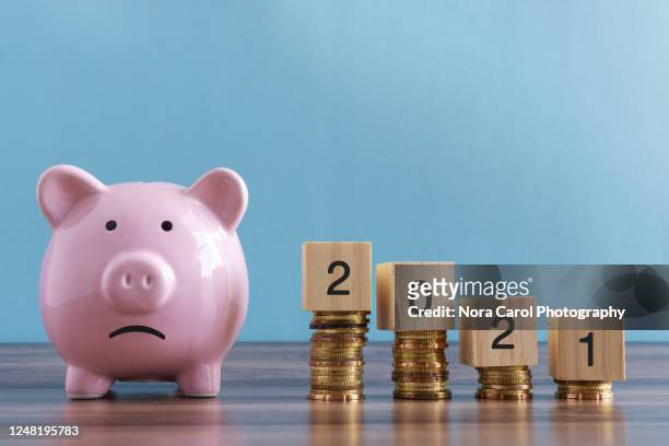 sad piggy bank and stack of coins 2021 - poverty reduction stock-fotos und bilder