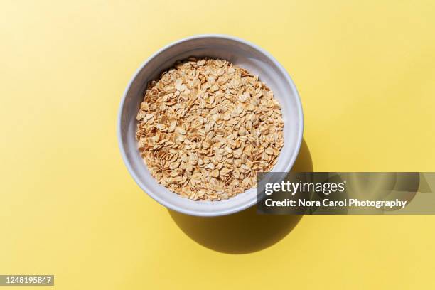 oat flakes in a bowl yellow background - oatmeal stock pictures, royalty-free photos & images