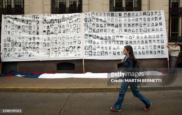 Una persona pasa frente a fotos de desaparecidos durante la dictadura de Augusto Pinochet, sostenidas por manifestantes frente al palacio de...