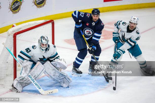 Nino Niederreiter of the Winnipeg Jets keeps an eye on the play between goaltender James Reimer and Marc-Edouard Vlasic of the San Jose Sharks during...