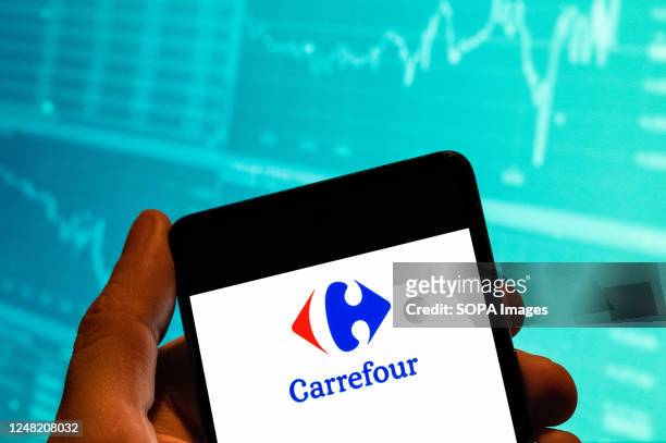 In this photo illustration, the French multinational supermarket chain Carrefour logo is seen displayed on a smartphone with an economic stock...