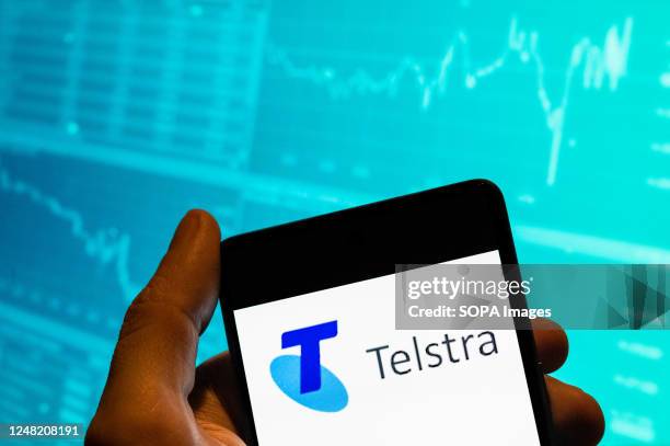 In this photo illustration, Australia's largest telecommunications company Telstra logo is seen displayed on a smartphone with an economic stock...