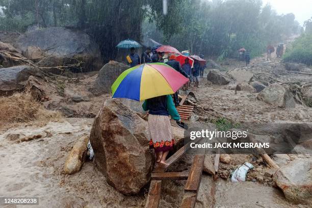 People walk across a makeshift bridge over flood water in Blantyre on March 14 caused by heavy rains following cyclone Freddy's landfall. - Cyclone...