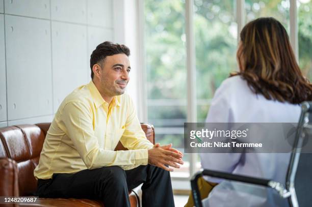 a senior man sits on a sofa with his therapist , discuss and gestures as his speaks to her. hopeful expression, mental health and counseling concept. - psychiatric hospital stockfoto's en -beelden