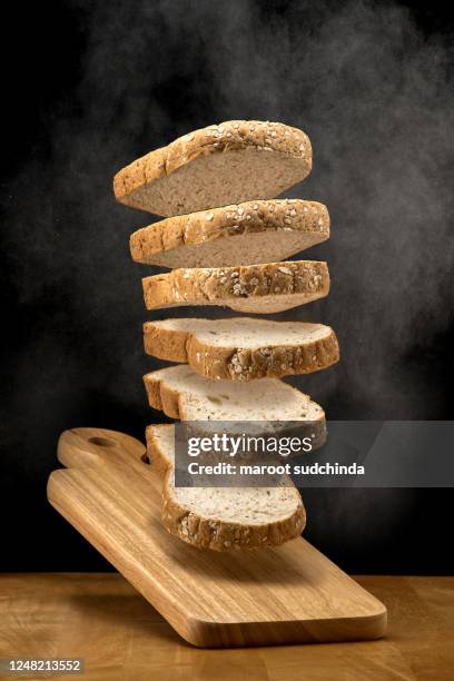 the conceptual picture of the whole wheat bread floating in the air on the line resembles that is about to fall on a wooden chopping block and the picture temporarily stops moving, on black background - sliced bread stock pictures, royalty-free photos & images