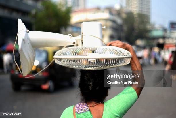 Woman carries a pedestal fan on her head during summer in Mumbai, India, 14 March, 2023. The India Meteorological Department declared a heatwave in...