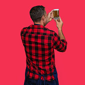 Caucasian male manual worker standing in front of colored background wearing button down shirt and holding craft beer