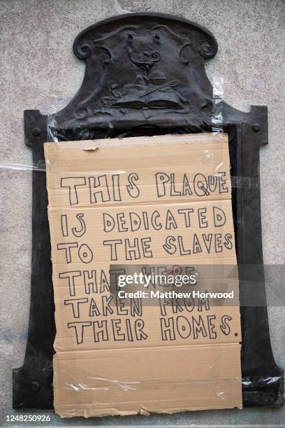 Close-up of the base of the Edward Colston statue plinth with a taped-on cardboard message saying "this plaque is dedicated to the slaves that were...