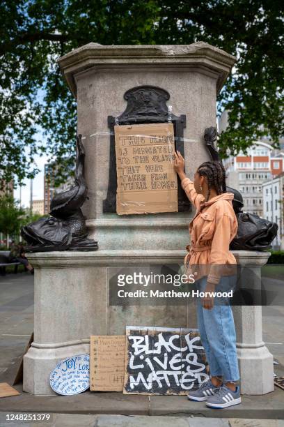 Asha poses for a photograph at the Edward Colston statue plinth where she a taped on a cardboard sign which says "this plaque is dedicated to the...