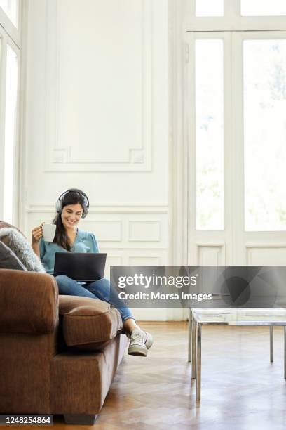 smiling woman holding cup while using laptop - familie sofa stock pictures, royalty-free photos & images