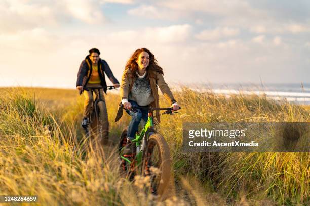 pareja joven montar bicicletas gordas en sendero costero - ciclismo fotografías e imágenes de stock