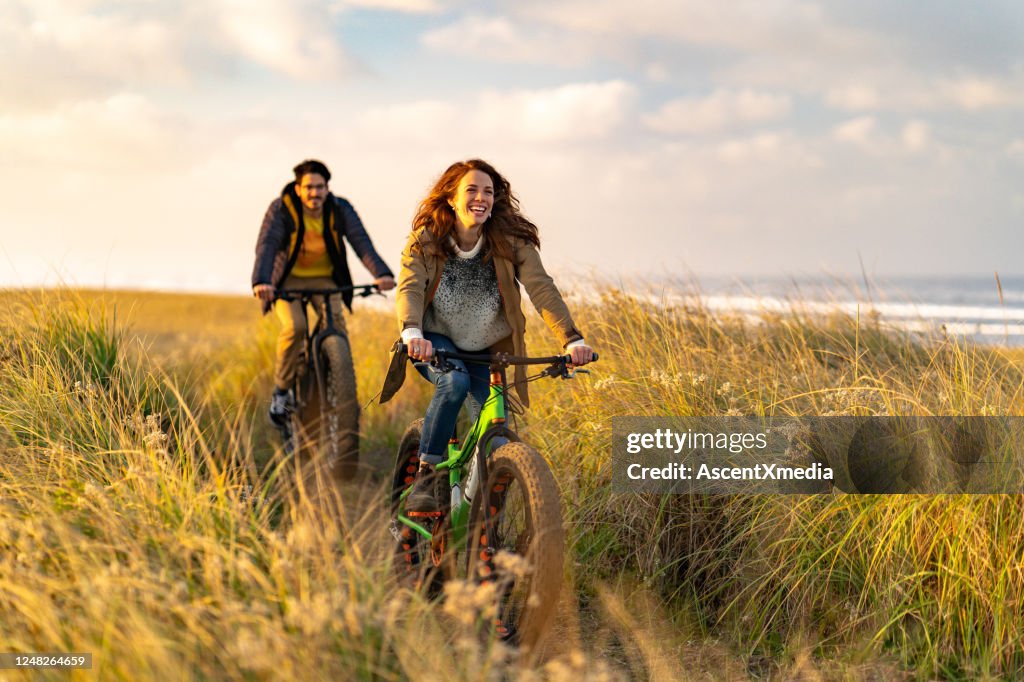 Young couple ride fat bikes on coastal trail